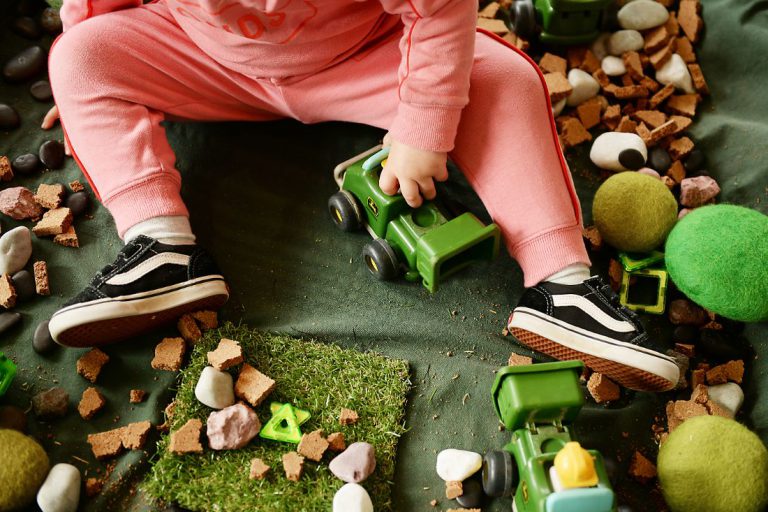 Evoke Clayton, image of child in pink trousers playing with green toy trucks